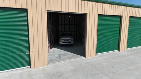Vehicle storage unit with a car parked inside and green roll-up doors.