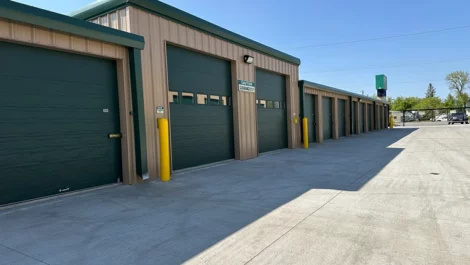 Row of storage units with green garage doors and yellow security bollards.