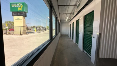 Hallway of storage units with green doors and a clear view of the exterior.