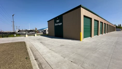 Exterior view of RV storage units with green doors and clear paved access.