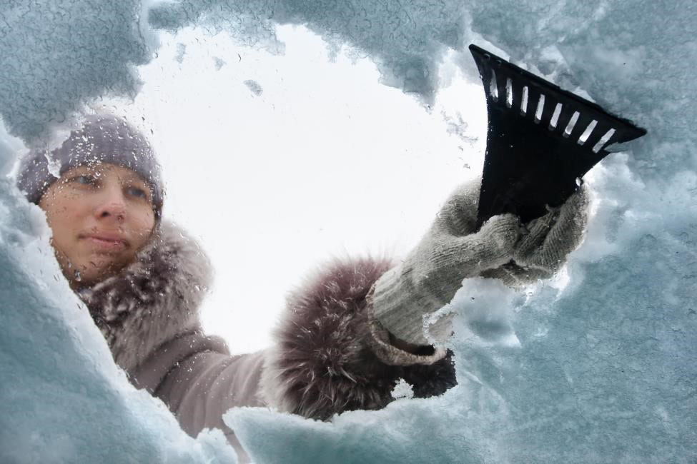 Woman using snow scraper to remove snow and ice from windshield.
