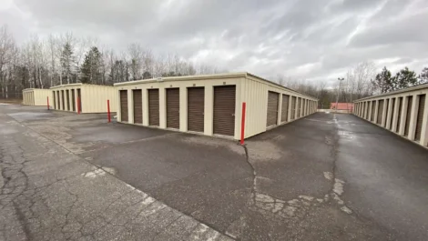 Storage facility with units along a paved path and red posts marking the entrance.