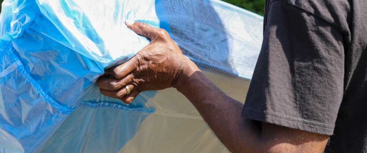 A man moves a mattress wrapped in a protective cover.