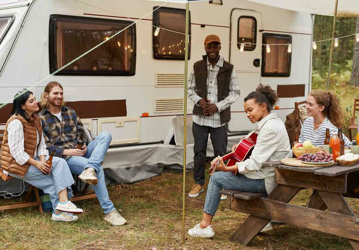A group of friends sit in a circle outside a camper