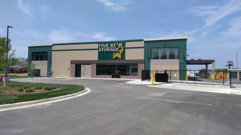 An outside view shows a green and tan self storage facility with a black gate in front.