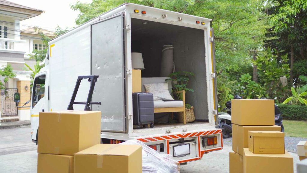 A moving truck with several boxes, a chair, and some other items as it’s being loaded.