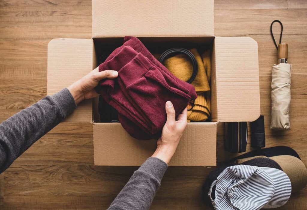 Someone placing items into a cardboard box to donate.