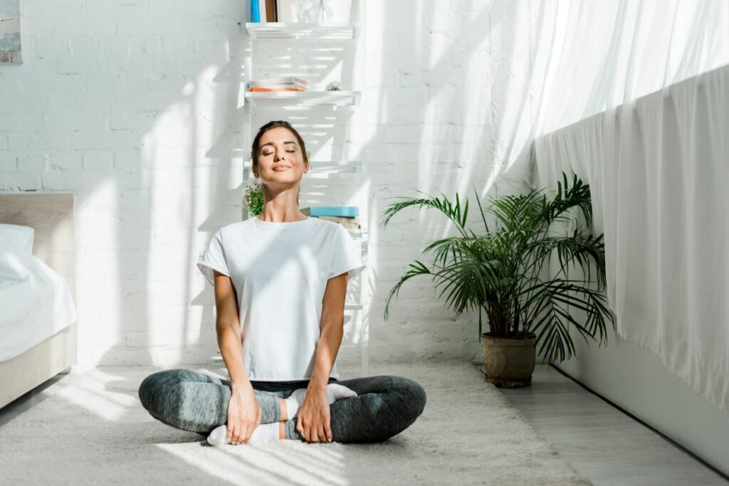 Young woman sitting with closed eyes and meditating in the bedroom.