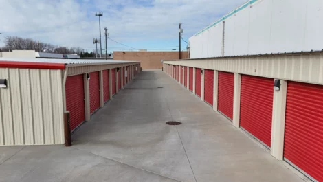 Row of red storage units with a wide paved path between them.