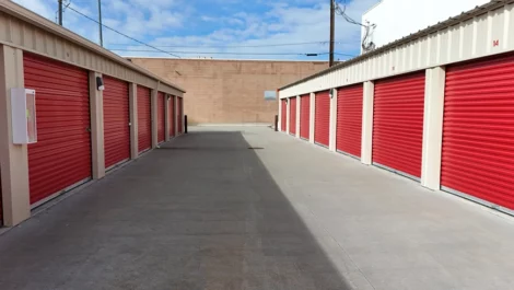 View of storage units with red doors and a wide paved driveway.