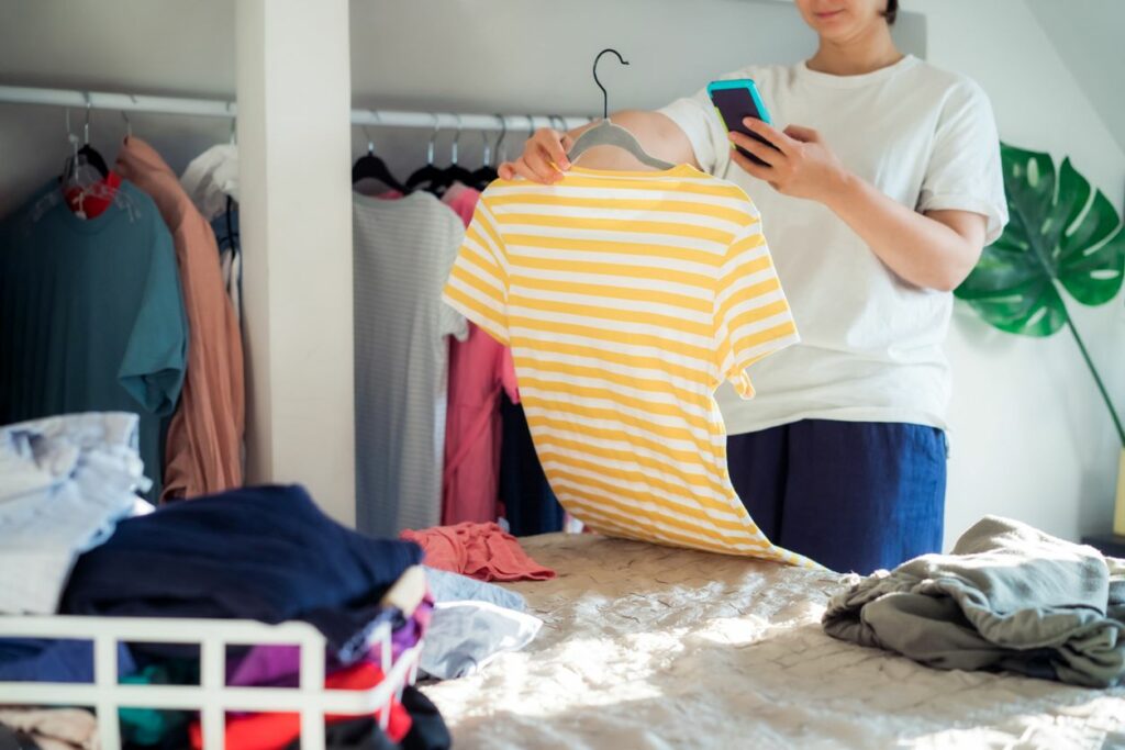 Woman taking a photo of a shirt while organizing clothes from the closet.