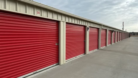 Storage units with red doors along a paved path and numbered for easy access.