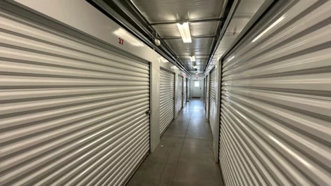Storage units along a hallway with metal roll-up doors and clear lighting.
