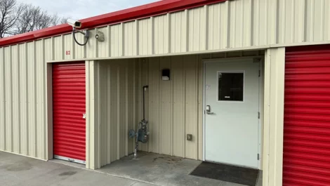 Self-storage unit with a red door and security camera next to the entrance.