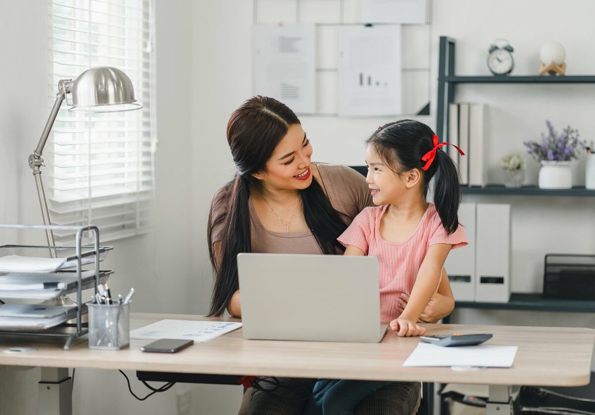 Smiling mother and daughter bonding at laptop in a home office.