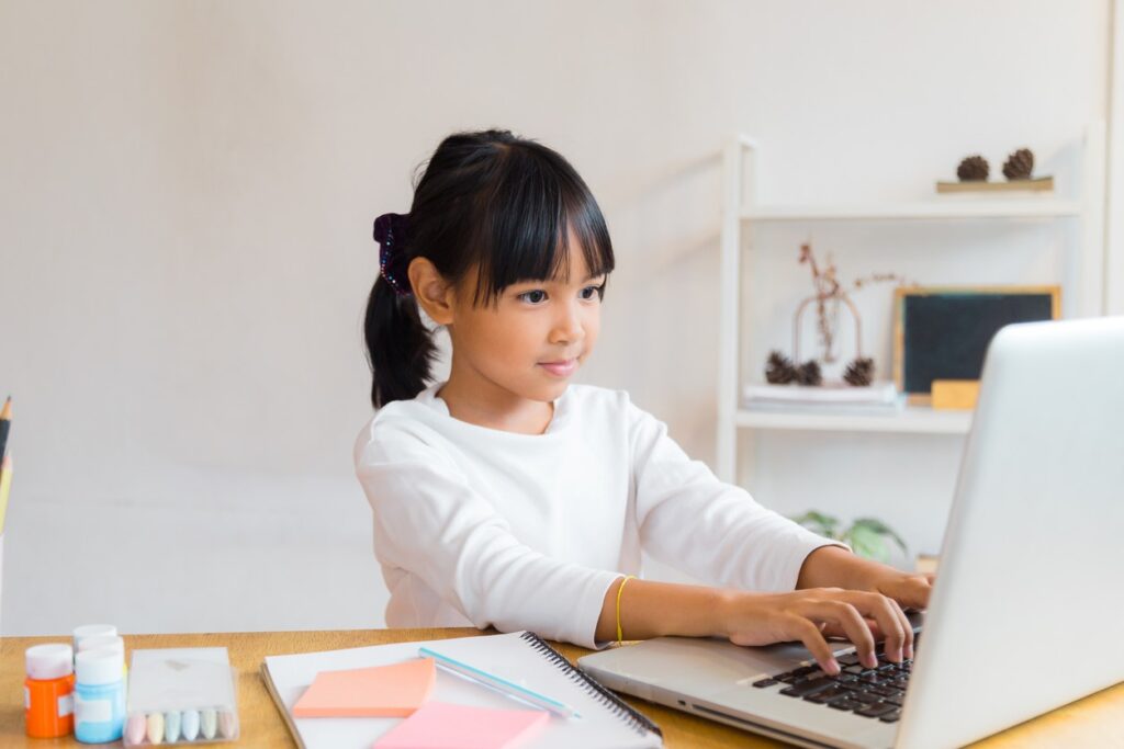 A young girl is working on homework on her laptop. 