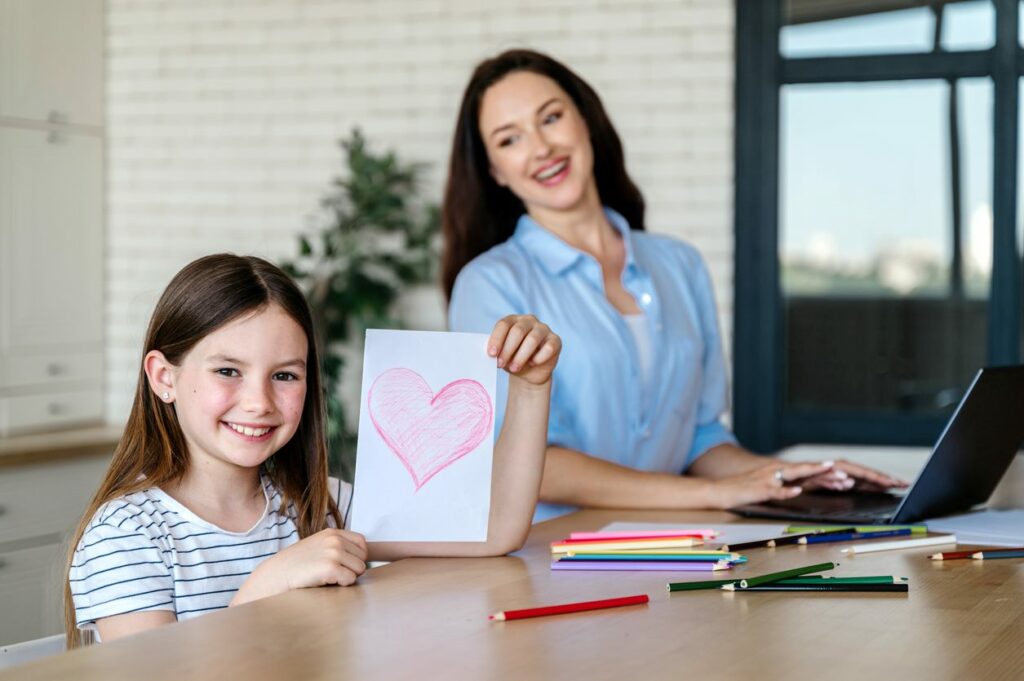 Mother and daughter working next to each other, with the daughter holding up a drawing.