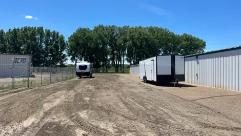 RV storage space with trailers parked on a gravel road surrounded by storage units.