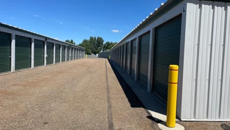Accessible storage unit path with yellow bollards and green roll-up doors.