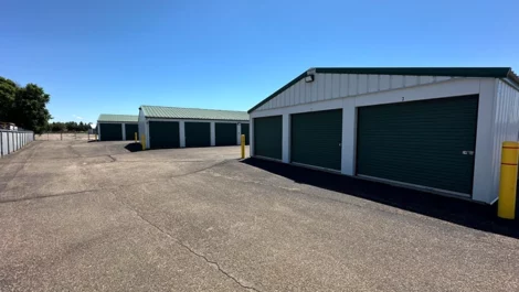 Storage units with roll-up doors and security bollards on a paved surface.