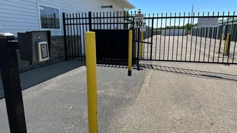 Security gate with keypad entry and yellow bollards access to a storage facility.