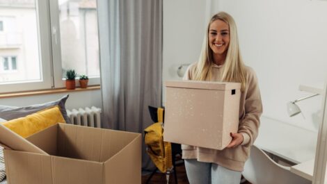 A college student smiles as she unpacks boxes of her items in her dorm room.