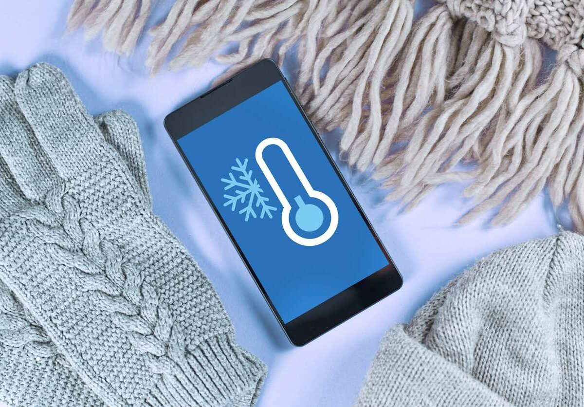 Knitted gloves, a scarf, and a hat nestled around a phone displaying a snowflake and blue thermometer.