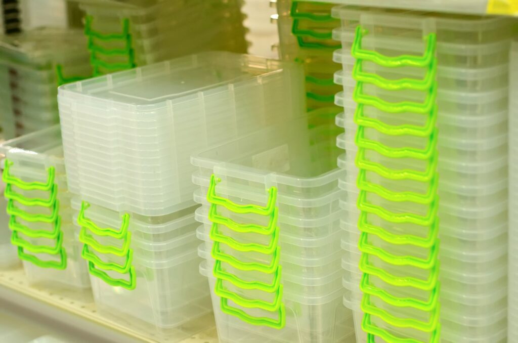 Plastic storage containers with green handles stacked into one another on a shelf. 