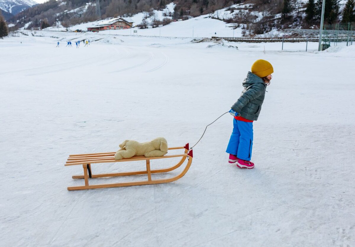 Toddler in colorful winter clothes pulling a sled with a stuffed animal through the snow.