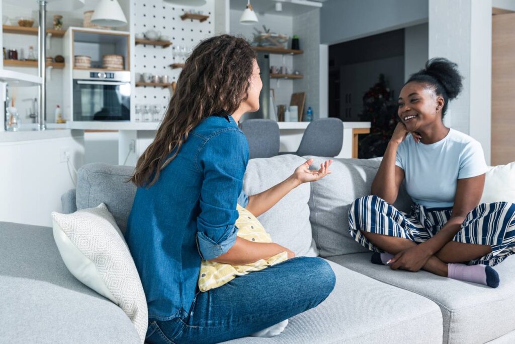 Two roommates are sitting on a couch in their apartment and sharing a pleasant conversation.