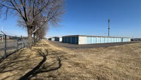 Storage units along a wide path with grass and trees nearby.