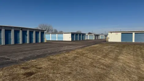 Storage units with blue doors lining a paved path and grassy area.