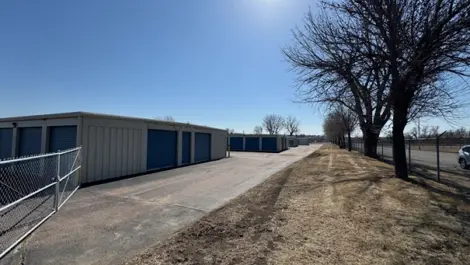 Storage units along a paved path with trees on one side and a fence on the other.