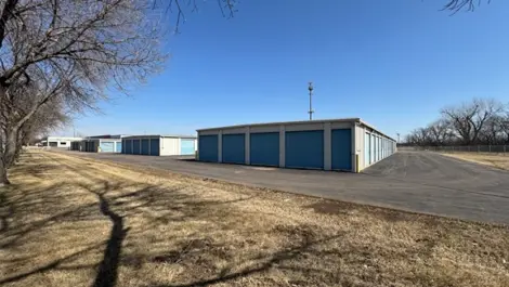 Row of storage units next to a paved road with open space.