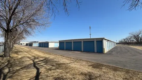 Storage facility with units along a path and trees on one side.