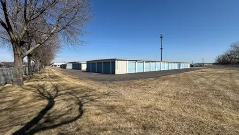 Storage units along a wide path with grass and trees nearby.