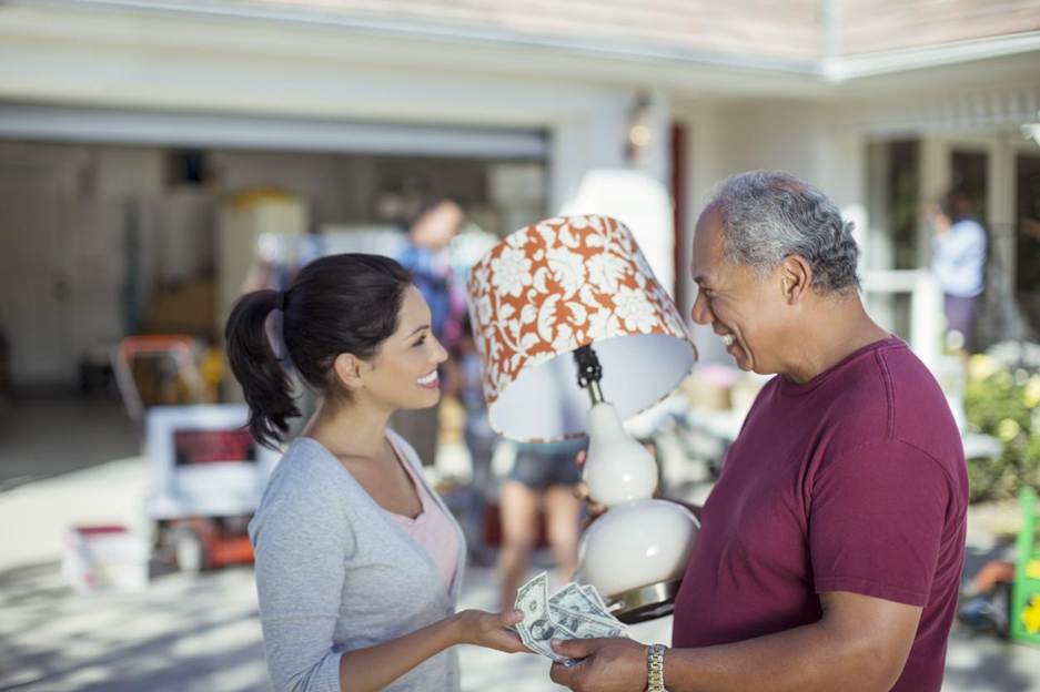 A man purchasing a lamp with cash from a woman at a yard sale. 