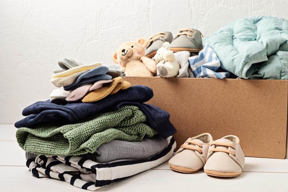 A set of baby clothes and toys folded and packed into a cardboard box. 