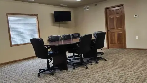 Meeting room with a large table chairs and a television on the wall.