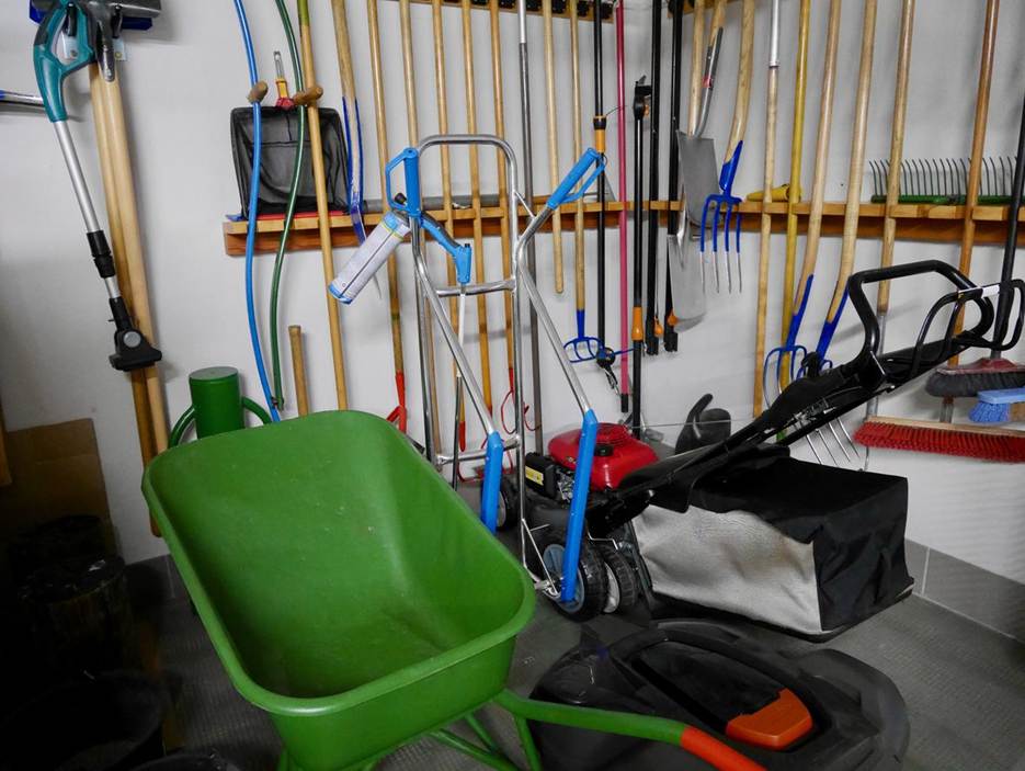 A set of garden tools hanging on a wall and tucked in the corner of a garage. 