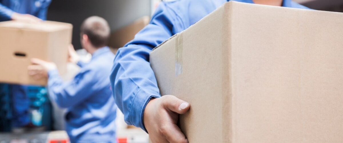 A group of workers in blue uniforms loads cardboard boxes into a moving truck.