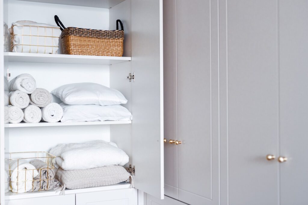 Several white towels, sheets, and pillows neatly folded and organized in an apartment cabinet.